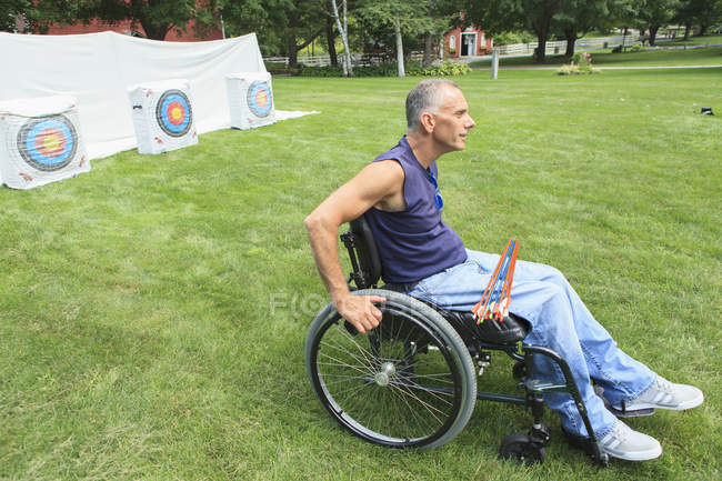 Человек с травмой спинного мозга в инвалидной коляске готовится к практике стрельбы из лука — стоковое фото