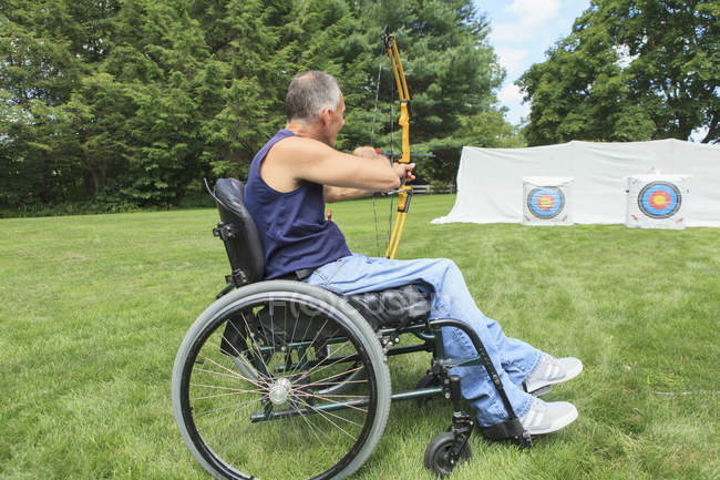 Uomo con lesione del midollo spinale in sedia a rotelle mira il suo arco e freccia per la pratica del tiro con l'arco — Foto stock