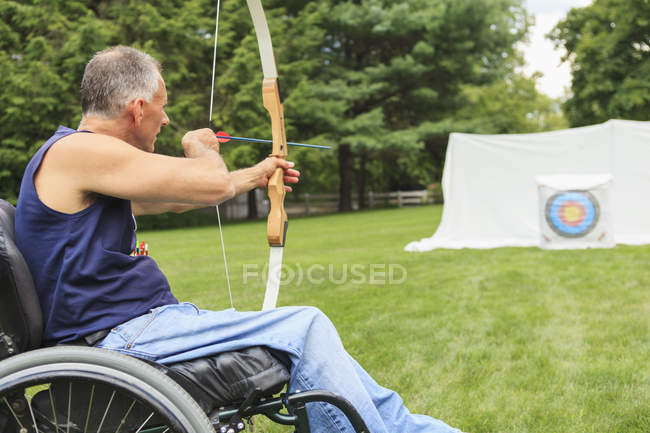Homem com lesão medular em cadeira de rodas visando seu arco e flecha para a prática de tiro com arco — Fotografia de Stock