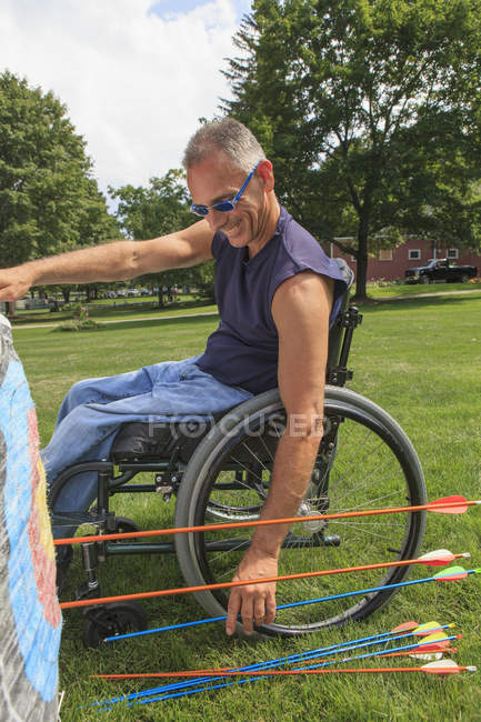 Человек с повреждением спинного мозга в инвалидной коляске удаляет стрелы из мишени после стрельбы из лука — стоковое фото