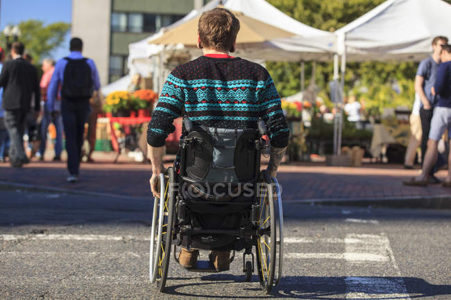 Hombre de moda con una lesión de médula espinal en silla de ruedas en un mercado al aire libre de la ciudad - foto de stock
