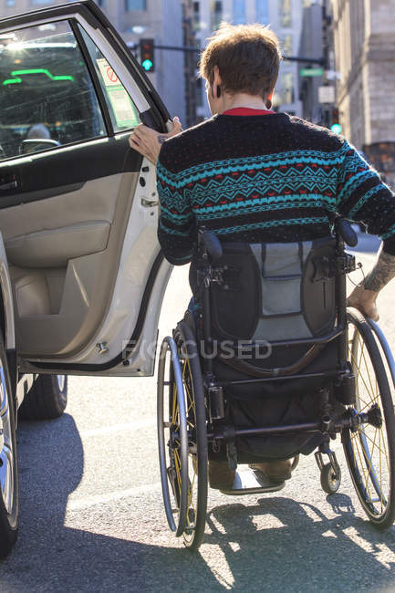 Trendy man with a spinal cord injury in wheelchair getting into a taxi cab — Stock Photo