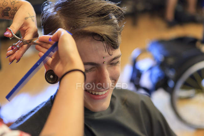 Homem na moda com uma lesão na medula espinhal em um salão de cabeleireiro recebendo um corte de cabelo — Fotografia de Stock