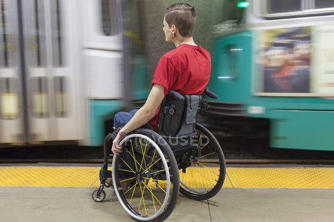 Модный человек с травмой спинного мозга в инвалидной коляске ждет поезда метро — стоковое фото