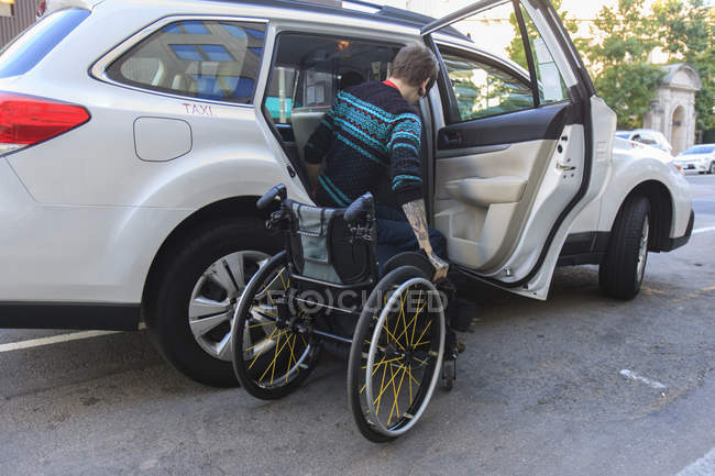 Homem na moda com uma lesão medular em cadeira de rodas entrando em um táxi — Fotografia de Stock