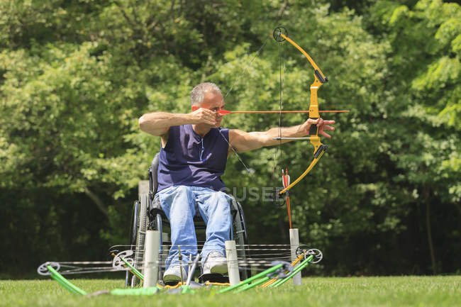Uomo con lesione del midollo spinale in sedia a rotelle mira il suo arco e freccia per la pratica del tiro con l'arco — Foto stock