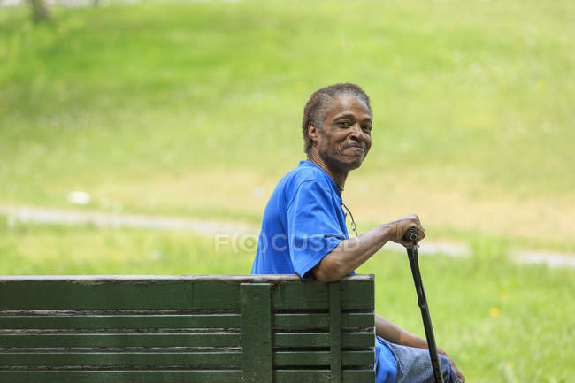 Homme avec traumatisme crânien relaxant avec sa canne dans un parc — Photo de stock