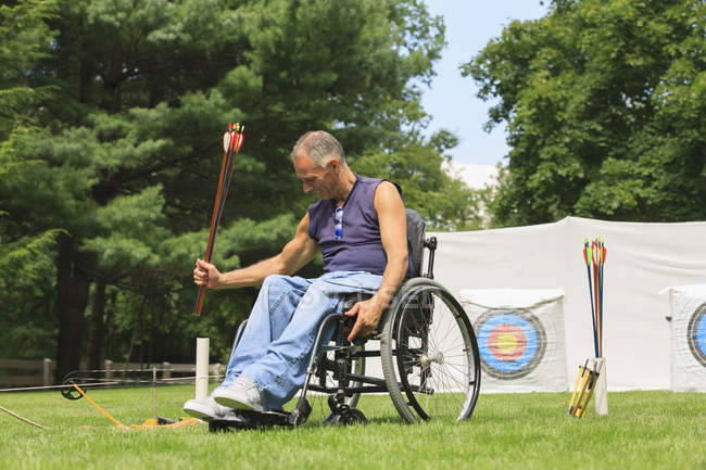 Homem com lesão medular em cadeira de rodas preparando-se para a prática de tiro com arco — Fotografia de Stock