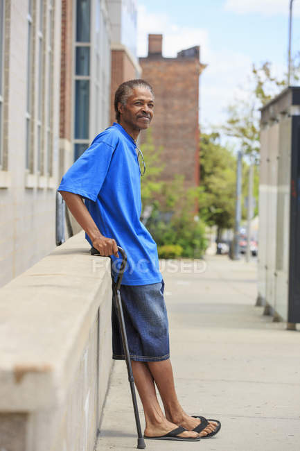 Hombre con lesión cerebral traumática relajándose con su bastón en su vecindario - foto de stock