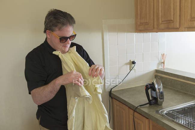 Man with congenital blindness folding his shirt after ironing it at home — Stock Photo