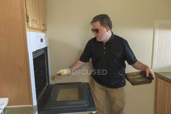 Man with congenital blindness using the oven in his kitchen — Stock Photo