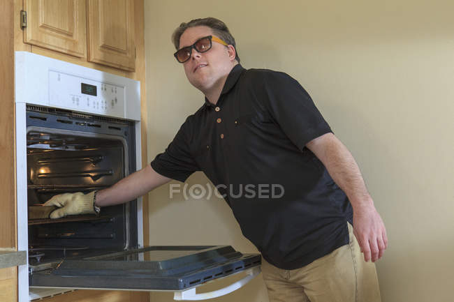 Man with congenital blindness using the oven in his kitchen — Stock Photo