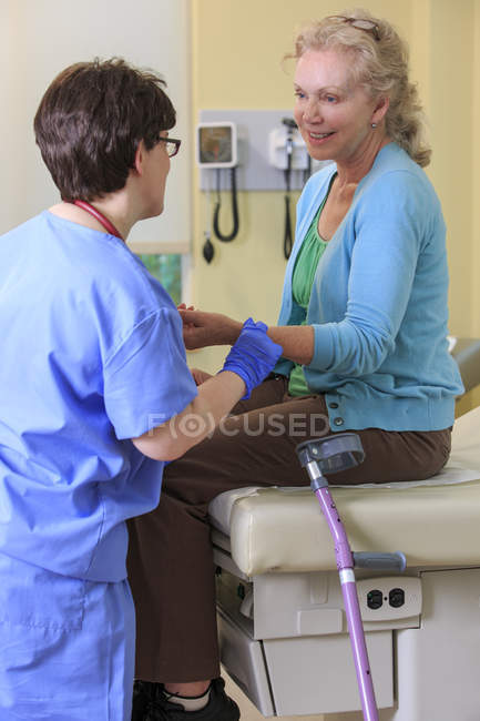 Enfermera con parálisis cerebral revisando el pulso de un paciente en una clínica - foto de stock
