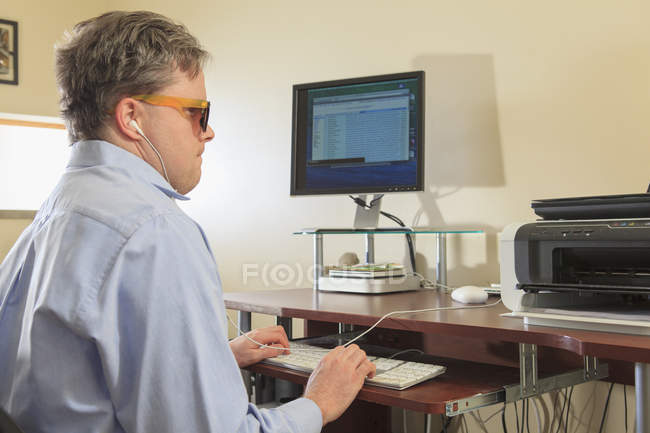 Человек с врожденной слепотой использует вспомогательные технологии за компьютером, чтобы слушать — стоковое фото