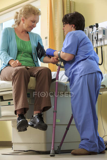 Enfermera con parálisis cerebral que toma la presión arterial de un paciente en una clínica - foto de stock