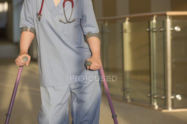 Enfermera con parálisis cerebral caminando por el pasillo de una clínica con sus bastones - foto de stock