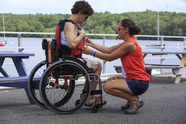 Mujer con una lesión en la médula espinal siendo ayudada por un instructor para usar un kayak - foto de stock