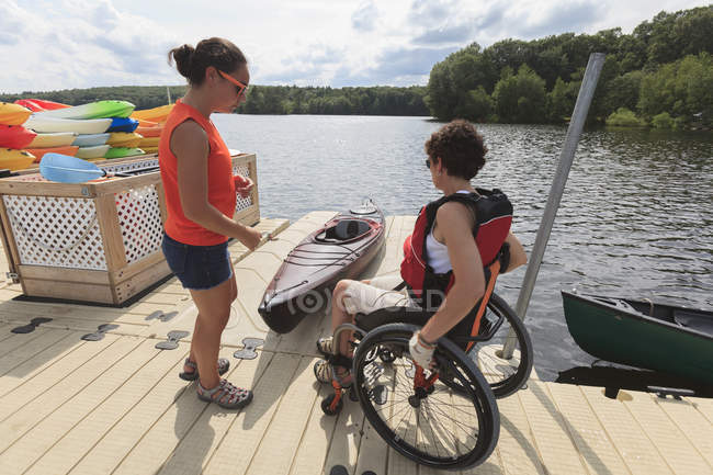 Instructor ayudando a una mujer con una lesión en la médula espinal con el uso de un kayak - foto de stock