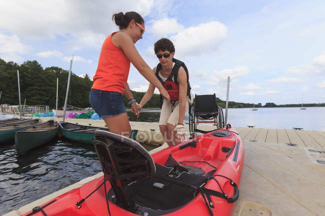 Istruttore aiutare una donna con una lesione del midollo spinale in un kayak dalla sua sedia a rotelle — Foto stock