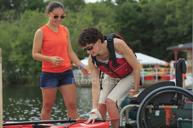 Instructor ayudando a una mujer con una lesión en la médula espinal con el uso de un kayak - foto de stock