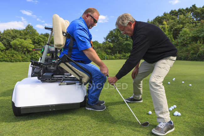 Людина з травмою спинного мозку в адаптивному візку в гольф кладе зелений з інструктором — стокове фото
