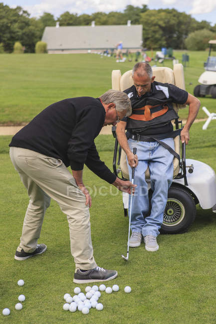 Man with spinal cord injury in an adaptive cart at golf putting green with an instructor — Stock Photo