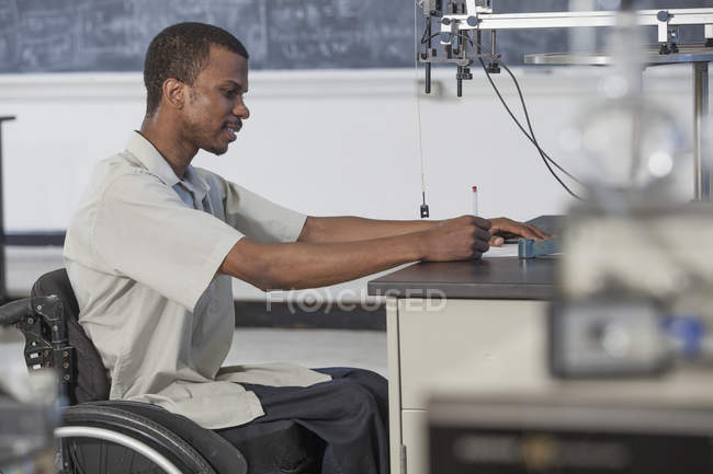 Студент з спінальним менінгітом у інвалідному візку вивчає прискорення на безфритовому столі в лабораторії. — стокове фото