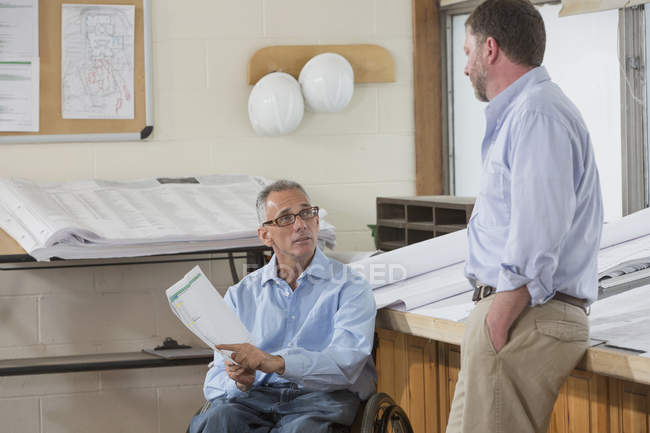 Два інженери проекту говорять про роботу, один в інвалідному візку з травмою спинного мозку — стокове фото