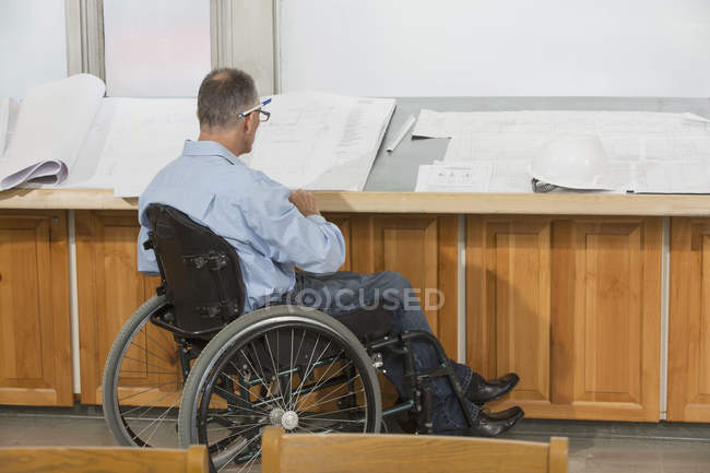 Инженер-проектировщик с травмой спинного мозга в инвалидной коляске, работающий над рисунками — стоковое фото