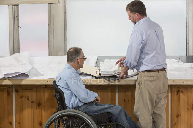 Два інженери проекту говорять про роботу, один в інвалідному візку з травмою спинного мозку — стокове фото