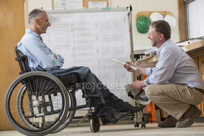 Dois engenheiros de projeto usando um rack de suspensão para planos de locais de trabalho, um em uma cadeira de rodas com uma lesão de medula espinhal — Fotografia de Stock