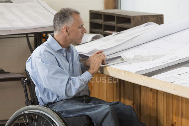 Engenheiro de projeto com uma lesão na coluna vertebral em uma cadeira de rodas trabalhando em seu tablet — Fotografia de Stock