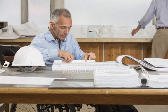 Two project engineers doing paperwork about the job, one in a wheelchair with a Spinal Cord Injury — Stock Photo