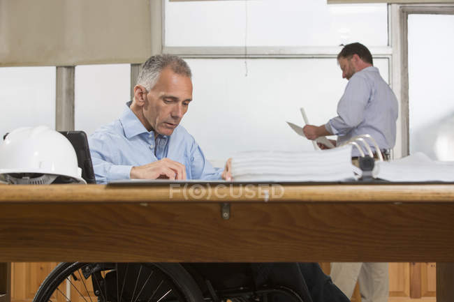 Due ingegneri del progetto stanno lavorando sul lavoro, uno su una sedia a rotelle con una lesione al midollo spinale. — Foto stock