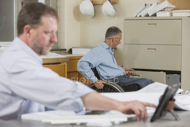 Zwei Projektingenieure im Baustellenbüro, einer im Rollstuhl mit Querschnittslähmung — Stockfoto