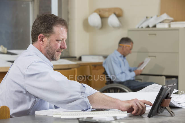 Two project engineers working at the job site office, one in a wheelchair with a Spinal Cord Injury — Stock Photo