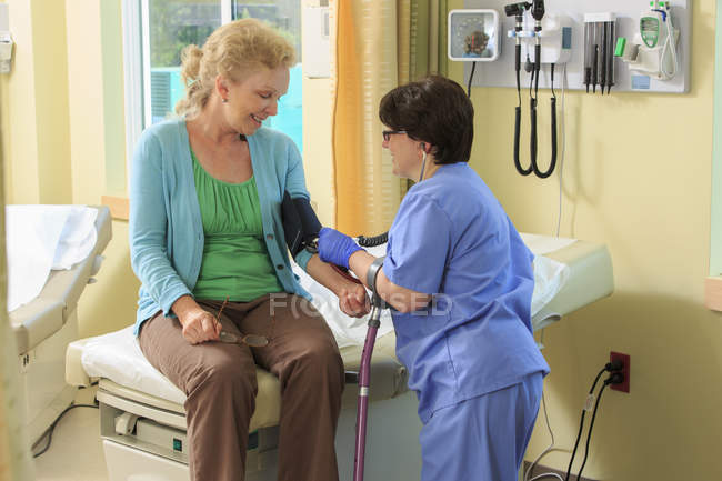 Enfermera con parálisis cerebral que toma la presión arterial de un paciente en una clínica - foto de stock