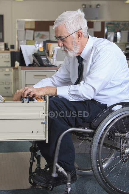Homem com Distrofia Muscular numa cadeira de rodas a preencher papéis na gaveta do escritório — Fotografia de Stock