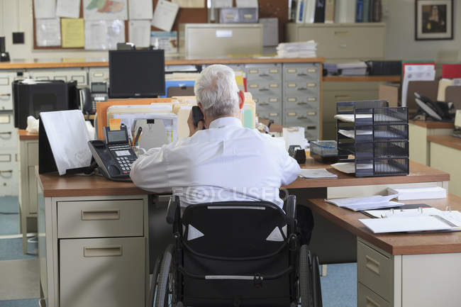 Чоловік з м'язовою дистрофією в інвалідному візку по телефону в своєму офісі — стокове фото