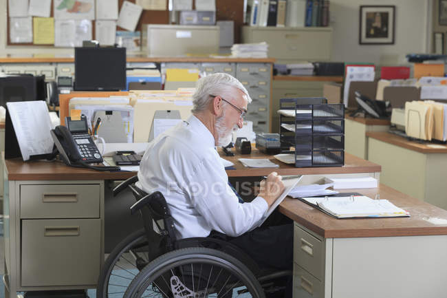 Homem com Distrofia Muscular em cadeira de rodas escrevendo em seu escritório — Fotografia de Stock