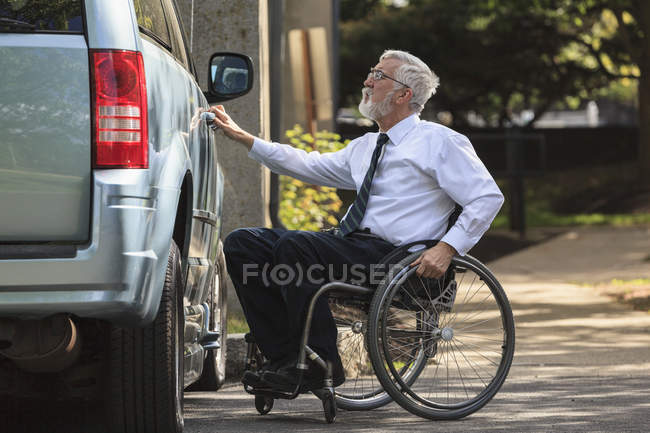 Hombre de negocios con distrofia muscular en silla de ruedas que entra en su furgoneta accesible en el estacionamiento - foto de stock