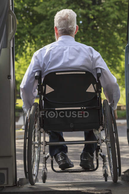 Homme d'affaires atteint de dystrophie musculaire en fauteuil roulant sortant de son van accessible dans le parking — Photo de stock