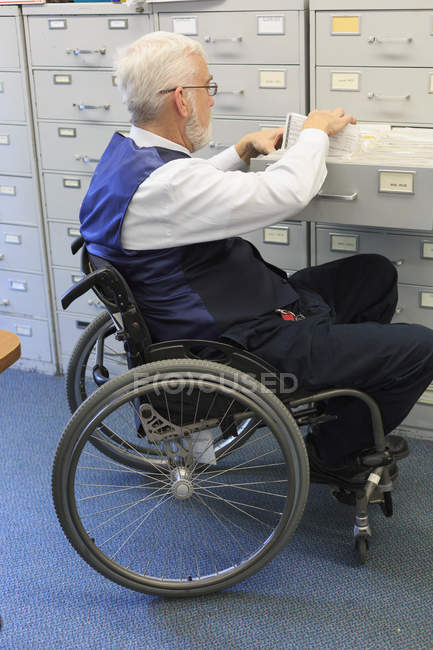 Mann mit Muskeldystrophie im Rollstuhl zieht Dokumente in Büro — Stockfoto