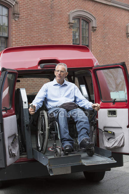 Hombre con una lesión en la médula espinal saliendo de una furgoneta accesible en un estacionamiento - foto de stock