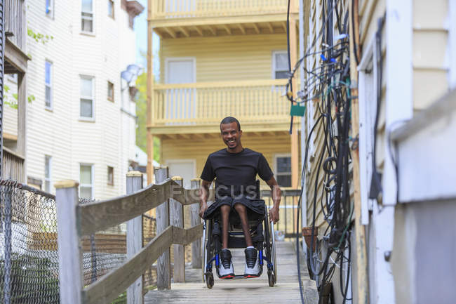 Hombre en silla de ruedas que tenía meningitis espinal en una rampa en su edificio de apartamentos - foto de stock