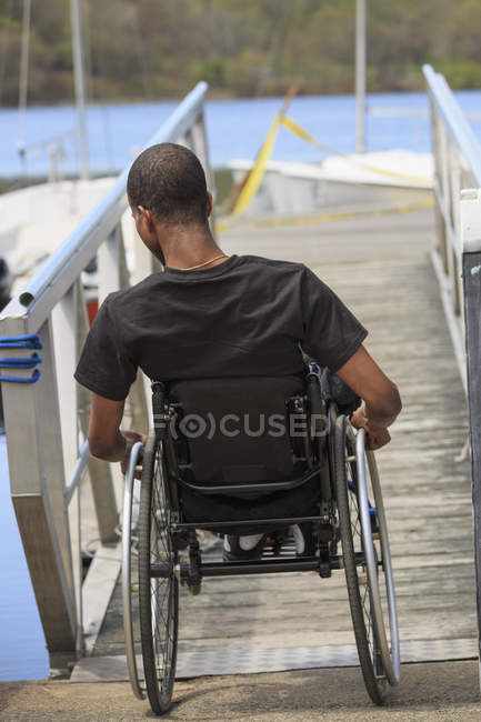 Homme en fauteuil roulant qui avait une méningite rachidienne descendant une rampe jusqu'à un quai — Photo de stock