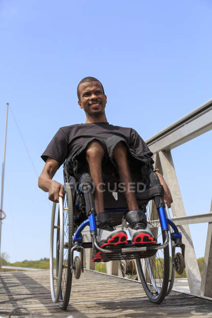 Hombre en silla de ruedas que tenía meningitis espinal bajando por una rampa a un muelle - foto de stock