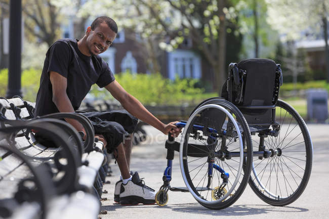Homme atteint de méningite rachidienne assis sur un banc près de son fauteuil roulant — Photo de stock