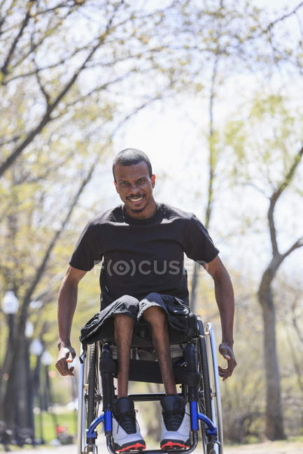Homem em uma cadeira de rodas que tinha meningite espinhal passando por um parque — Fotografia de Stock
