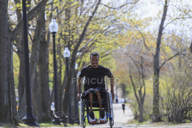 Homem em uma cadeira de rodas que tinha meningite espinhal passando por um parque — Fotografia de Stock